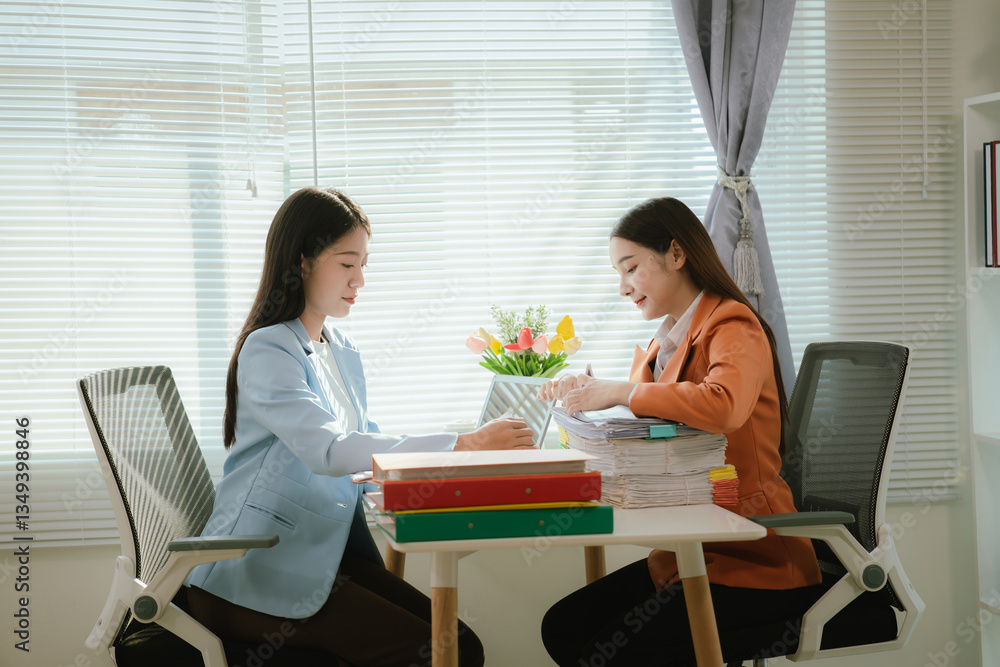 Two stressed businesswomen sit at a desk, covered in documents. Two stressed businesswomen sit at a desk, covered in documents.