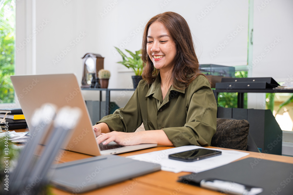 Obraz premium Happy beautiful female sitting indoors on desk shopping online, meeting on computer, remote work, Asian young business woman freelancer working with laptop computer and calculator at home office