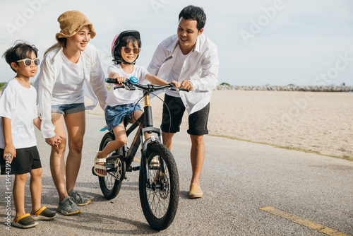 In warm glow of a summer sunset a happy father mother and son enjoy a road trip on a sandy beach. Teaching and learning bicycle riding create a cheerful tourism day concept filled with smiles and joy.