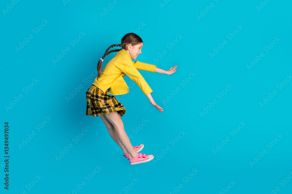 Obraz premium Young cute girl with braided hair in stylish outfit posing playfully against a bright blue background, radiating happiness, youthfulness
