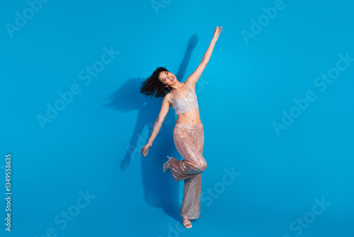 Wallpaper Mural Young stylish woman in sparkling outfit posing excitedly with arms raised against a vibrant blue background Torontodigital.ca