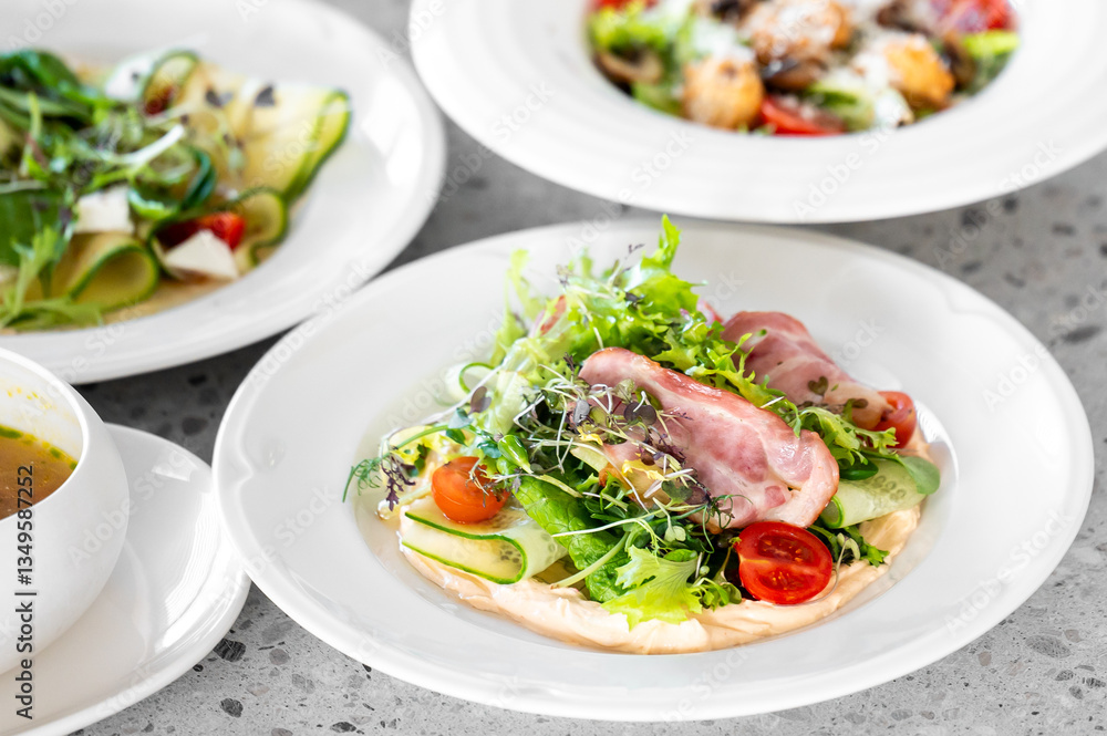A fresh mixed salad featuring cherry tomatoes, cucumber ribbons, and ham slices on a white plate, with other dishes in the background. Perfect for healthy eating concepts. A fresh mixed salad featuring cherry tomatoes, cucumber ribbons, and ham slices on a white plate, with other dishes in the background. Perfect for healthy eating concepts.