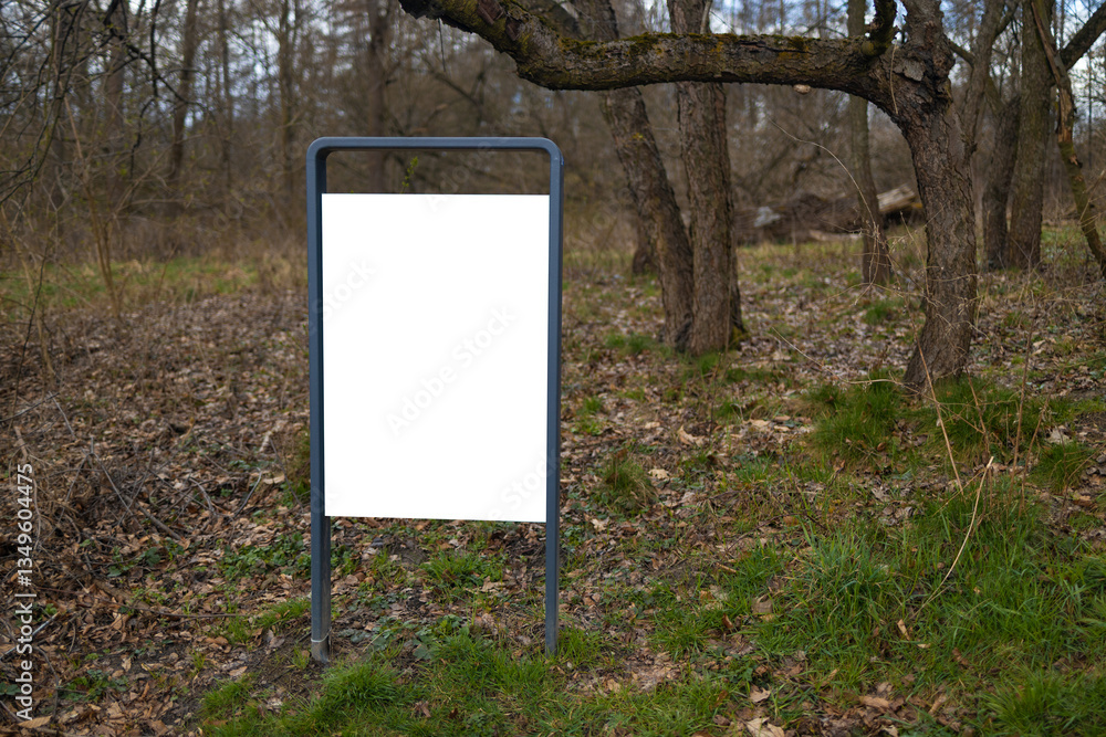A blank billboard in the forest, standing amidst trees and nature. The empty signboard provides a space for future advertisements, blending with the natural surroundings of the park or woods.