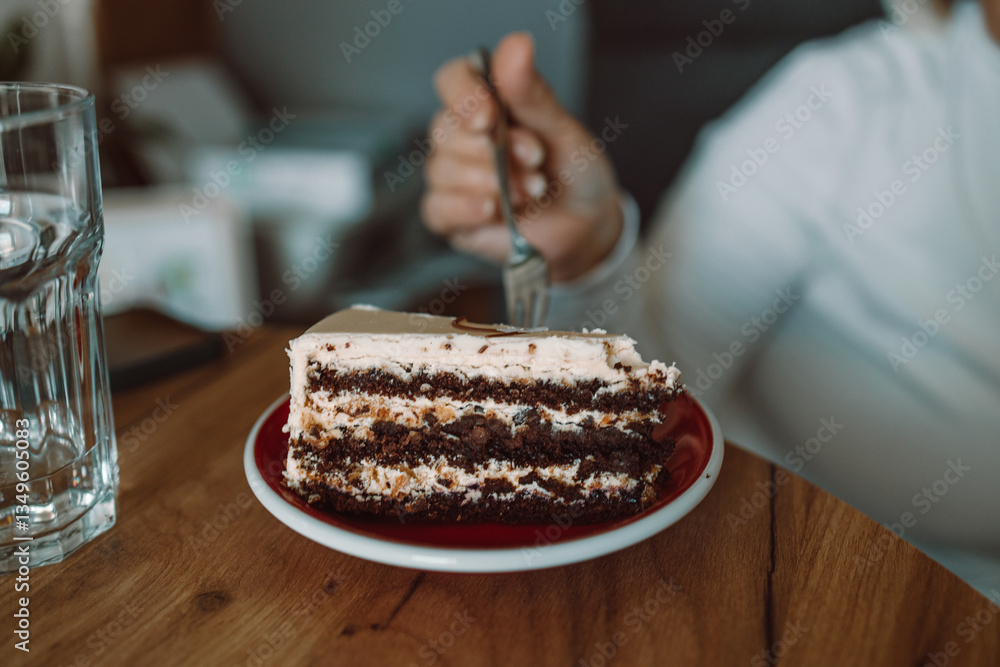 A close-up of a person eating a delicious slice of cake topped with cream, using a fork. The image captures a cozy, relaxed moment of enjoying a sweet dessert at a wooden table.