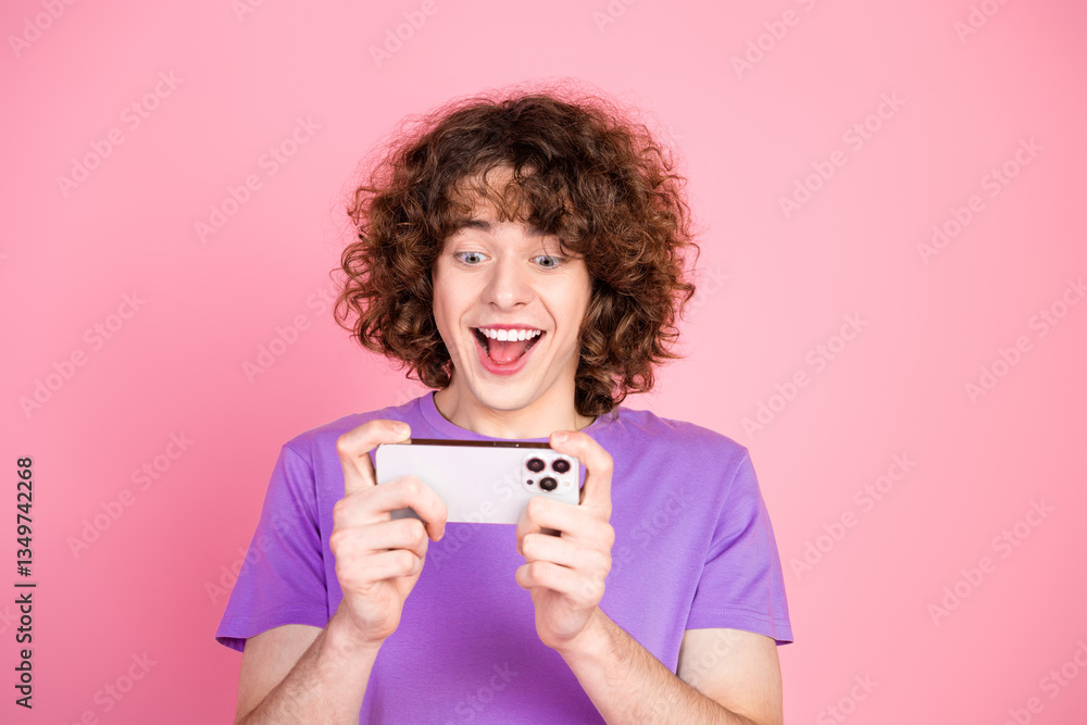 Delighted young man playing on smartphone with excitement and fun, joyful expression on pink background Delighted young man playing on smartphone with excitement and fun, joyful expression on pink background