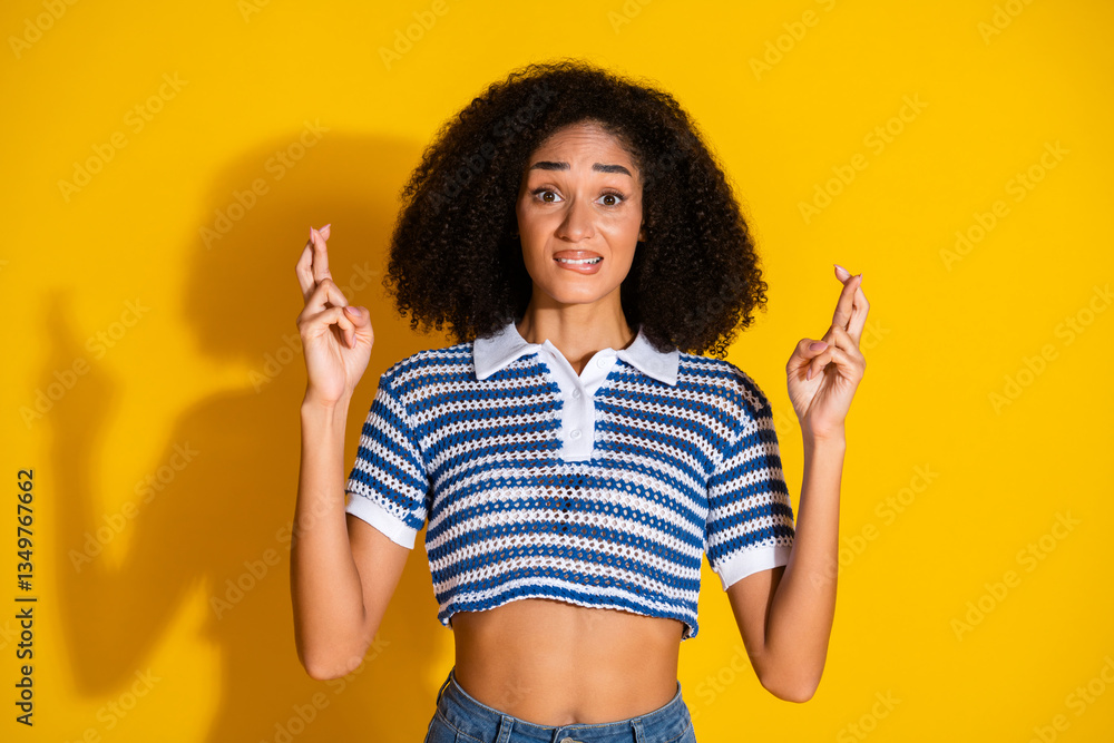 Φωτογραφία Young stylish woman with curly hair showing finger crossed gesture on yellow background in casual striped polo shirt
