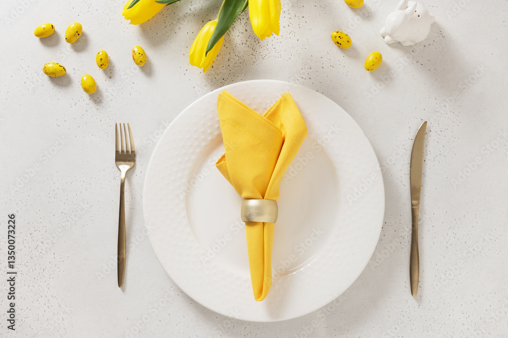 Easter table setting with spring tulips, white plates, bunny, eggs and yellow decoration on white background. Happy Easter celebration. Copy space. View from above.