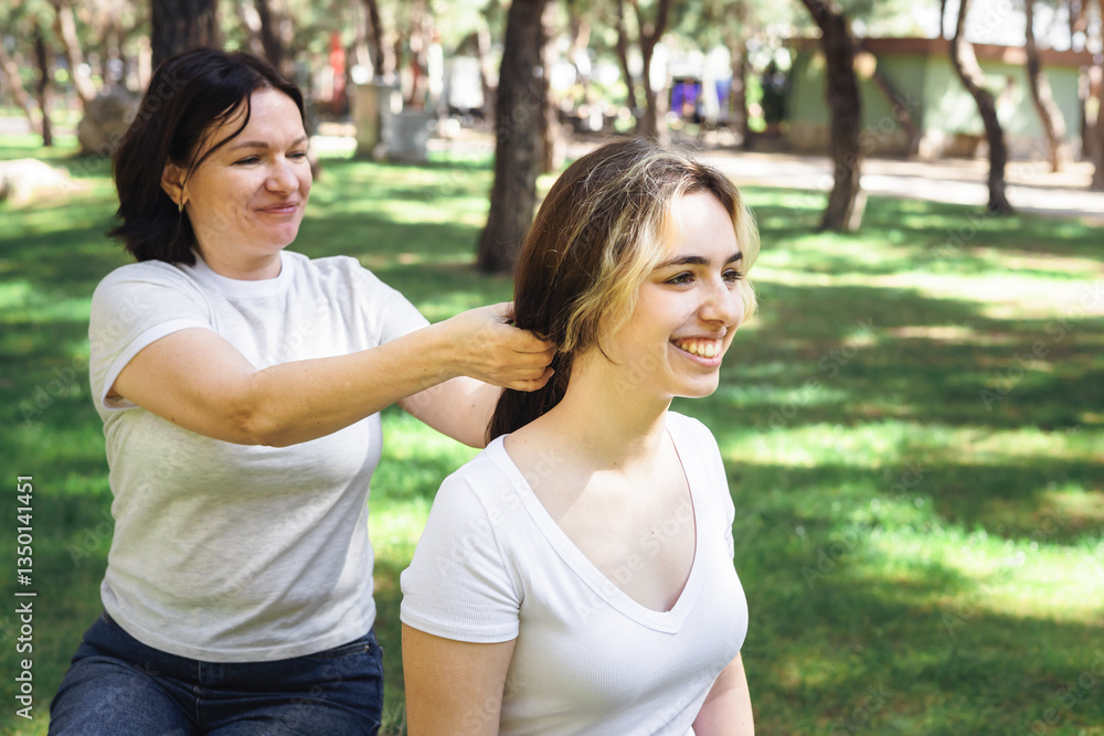 Two women enjoy a sunny afternoon in a park while one styles the other's hair Two women enjoy a sunny afternoon in a park while one styles the other's hair