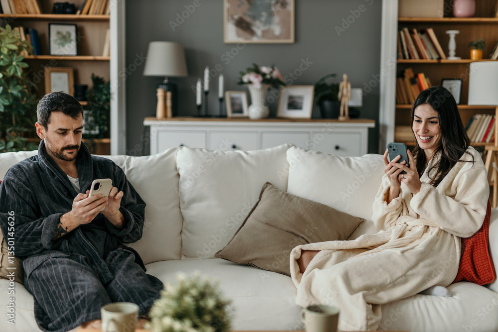 Fototapeta premium Couple relaxing on sofa using smartphones in modern apartment