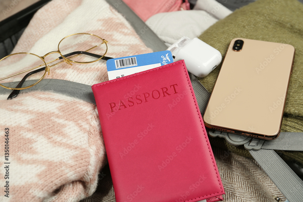 Passport with ticket, smartphone, earphones and glasses on packed suitcase, closeup