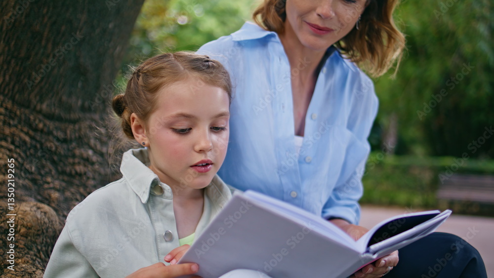 Fototapeta premium Little child reading fairytale for mom in park closeup. Mother kid enjoying book