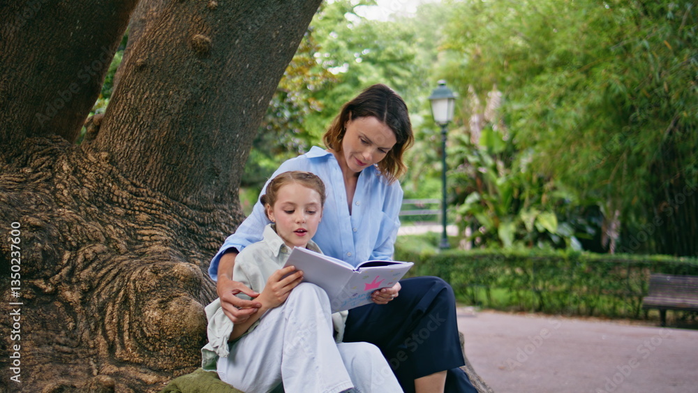 Naklejka premium Mom kid enjoying novel together at summer garden. Mother daughter reading book