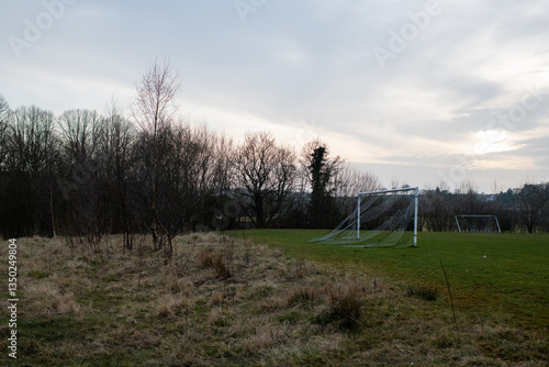 Eham A soccer field with a goal and a few trees in the background. The sky is cloudy and the grass is dry