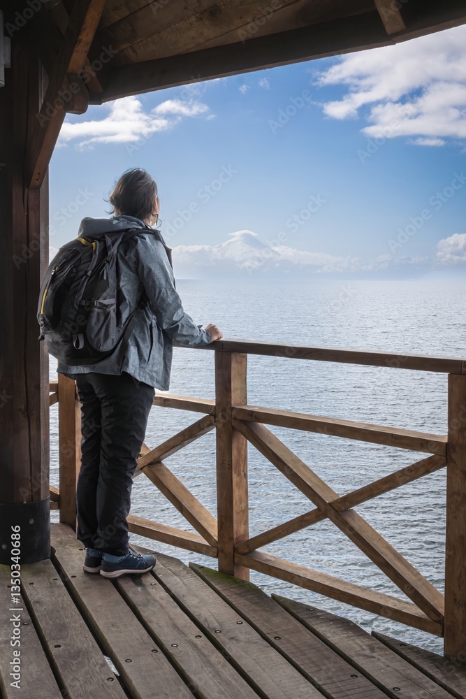 backpacking young woman traveler viewing a snow-capped mountaintop from a pier. Traveler in Osorno Volcano backpacking young woman traveler viewing a snow-capped mountaintop from a pier. Traveler in Osorno Volcano