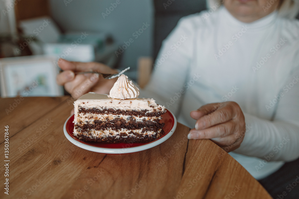 A close-up of a person eating a delicious slice of cake topped with cream, using a fork. The image captures a cozy, relaxed moment of enjoying a sweet dessert at a wooden table.
