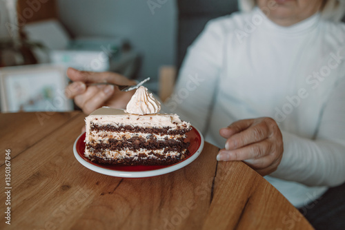 Obraz na płótnie A close-up of a person eating a delicious slice of cake topped with cream, using a fork. The image captures a cozy, relaxed moment of enjoying a sweet dessert at a wooden table. w salonie