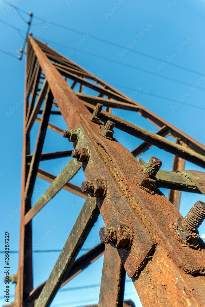 Rusted power line tower against clear blue sky demonstrates effects of weathering over time Rusted power line tower against clear blue sky demonstrates effects of weathering over time