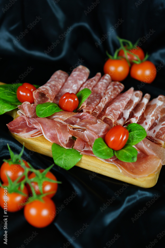 Flat lay of italian charcuterie selection on wooden board with fresh basil and cherry tomatoes, elegant food styling, catering, restaurant concept Flat lay of italian charcuterie selection on wooden board with fresh basil and cherry tomatoes, elegant food styling, catering, restaurant concept