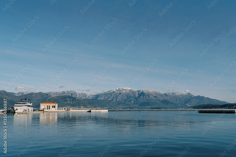 Naklejka premium Motor yacht moored to a pier with a small building in the background of a mountain range