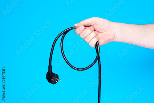 Hand holding black power cable on blue background.