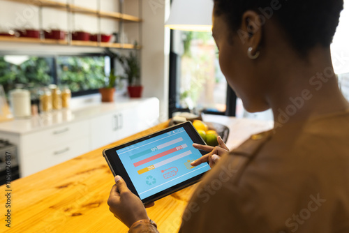 African American woman using tablet to monitor energy usage in modern kitchen
