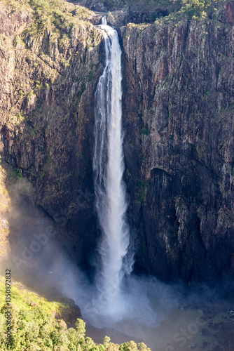 Wallaman Falls, Queensland, is Australia's tallest single-drop waterfall, surrounded by lush rainforest, cascading dramatically under a bright, sunny sky. A stunning natural landmark.