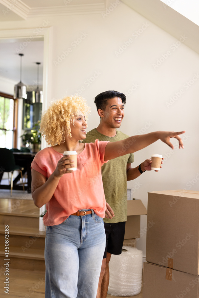 Young diverse couple enjoying coffee while unpacking in new home, smiling and pointing Young diverse couple enjoying coffee while unpacking in new home, smiling and pointing