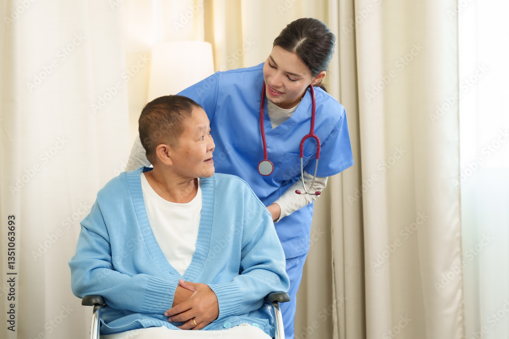 Fototapeta premium Caucasian female physiotherapist in blue medical scrubs standing behind Asian senior female cancer patient sitting in wheelchair smiling during supportive home care therapy session
