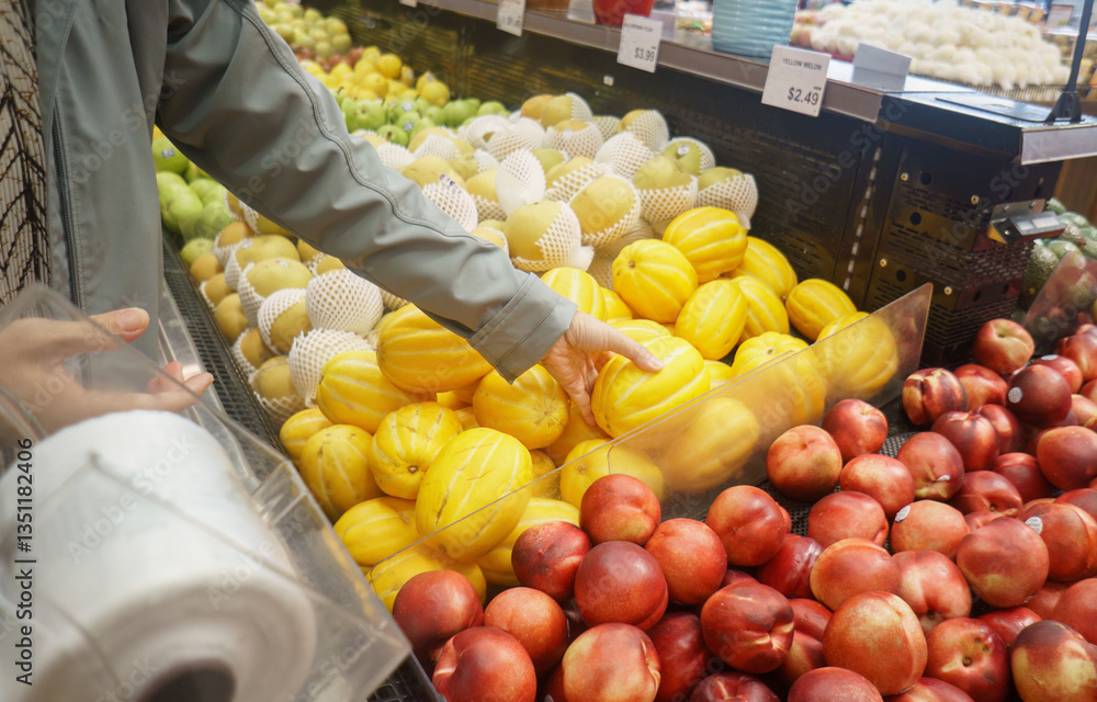 Woman choosing yellow melon at the supermarket. Customer buying fresh fruit at grocery shop. California.
