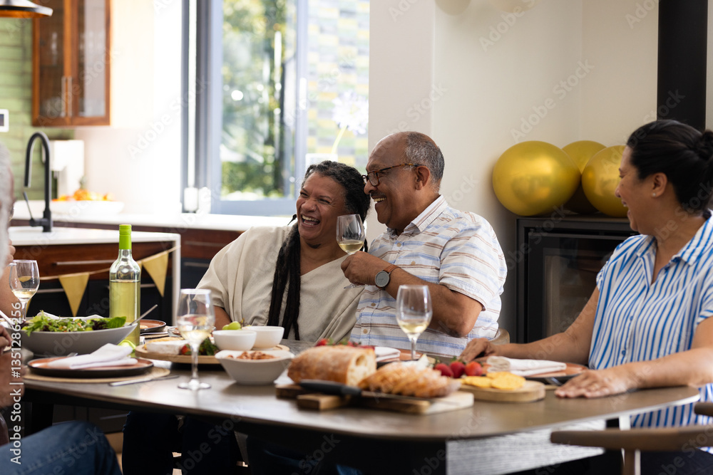 Diverse senior friends enjoying laughter and wine at home during cozy meal Diverse senior friends enjoying laughter and wine at home during cozy meal