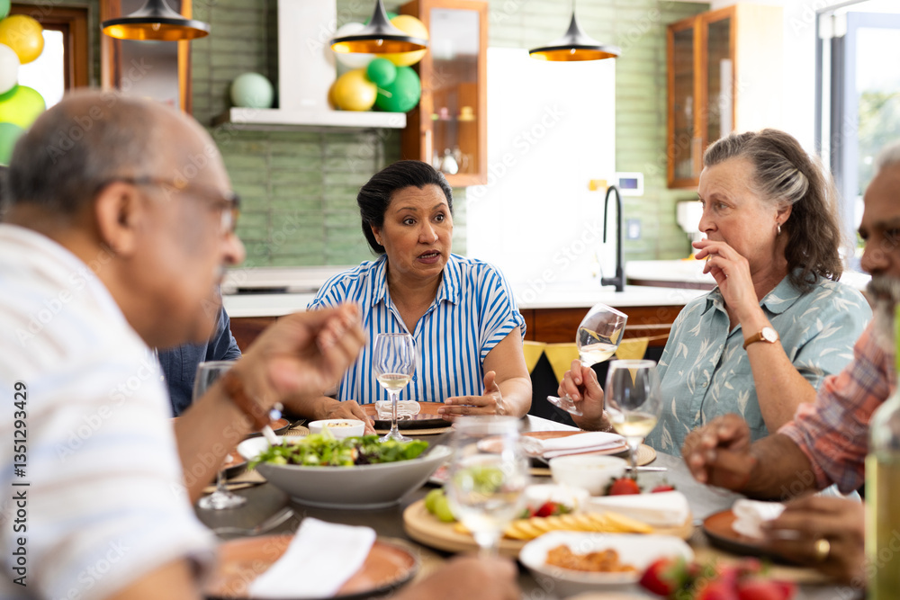 Diverse senior friends enjoying conversation and wine around dining table at home Diverse senior friends enjoying conversation and wine around dining table at home