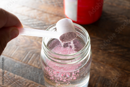 A view of a hand scooping electrolyte powder into a glass of water.