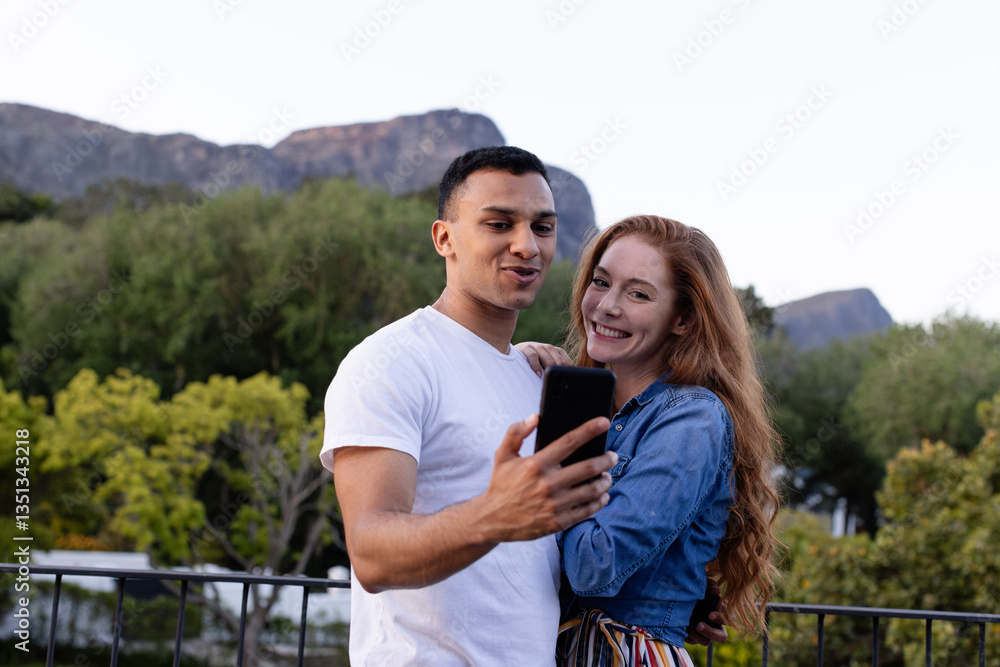 Young diverse couple smiling and taking selfie in garden with scenic mountain view Young diverse couple smiling and taking selfie in garden with scenic mountain view