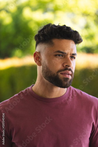 Young man in casual shirt standing outdoors, looking thoughtful in nature