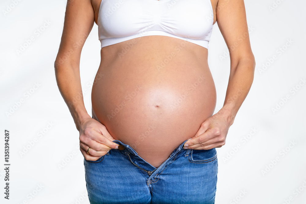 Front view of a pregnant woman with a big belly trying to put on a trouser on white background