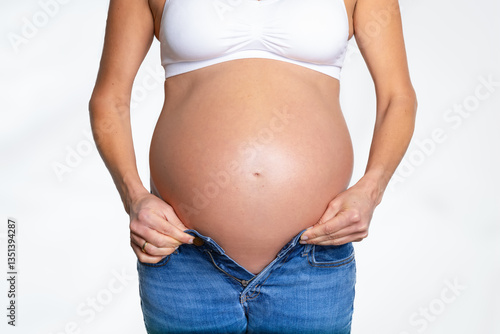 Obraz na płótnie Front view of a pregnant woman with a big belly trying to put on a trouser on white background w salonie
