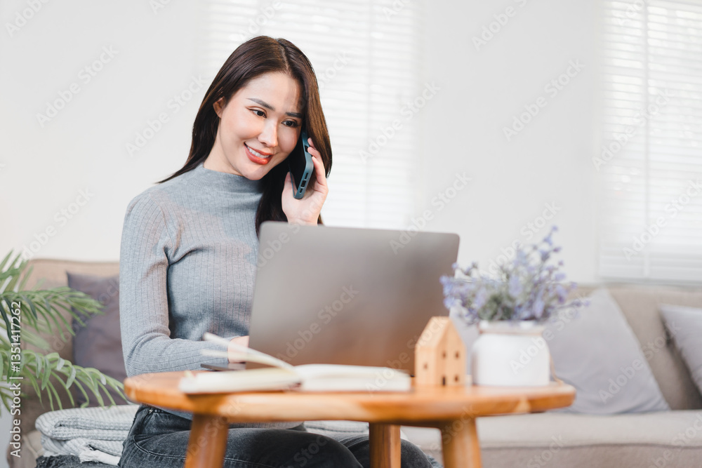 Asian businesswoman smiling while talking on phone and working on laptop in cozy home office setting. Asian businesswoman smiling while talking on phone and working on laptop in cozy home office setting.