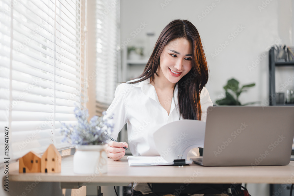 Asian businesswoman working happily at her desk with laptop and documents in bright modern office. Asian businesswoman working happily at her desk with laptop and documents in bright modern office.
