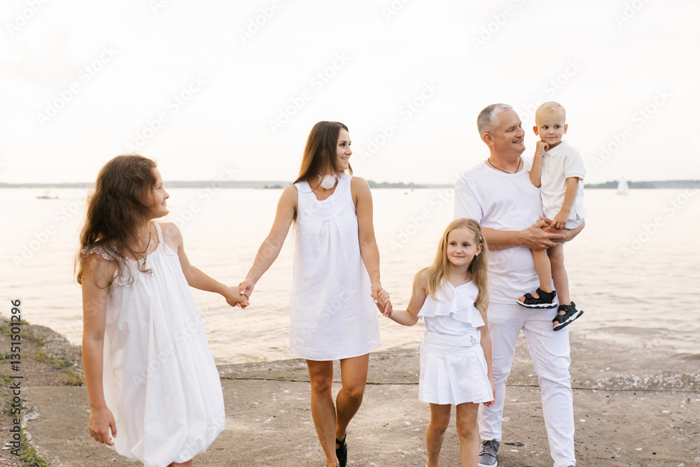 Happy family of five is walking on beach, with daddy holding baby