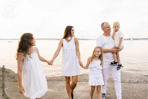 Obraz na płótnie Happy family of five is walking on beach, with daddy holding baby w salonie