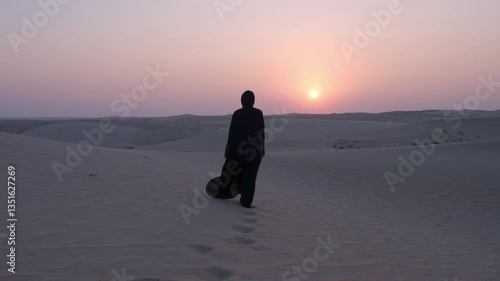 Arabic woman lady with Abaya cloth slow motion standing walking
 looking at the sun in the desert sand dune sunset

