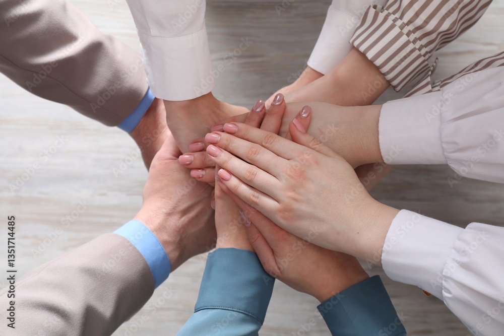 Business concept. Group of people stacking hands at light wooden table, top view Business concept. Group of people stacking hands at light wooden table, top view