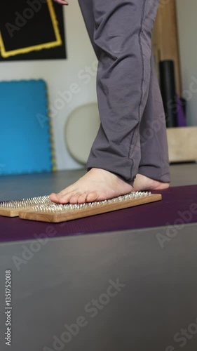 Foot standing on nail board for balance and relaxation, wooden spike mat on yoga floor, acupressure therapy session in vertical video