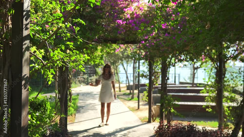 A smiling woman in a white dress and sunglasses walks through a sunlit garden, admiring blooming flowers and lush greenery, enjoying the peaceful atmosphere and natural beauty. A smiling woman in a white dress and sunglasses walks through a sunlit garden, admiring blooming flowers and lush greenery, enjoying the peaceful atmosphere and natural beauty.