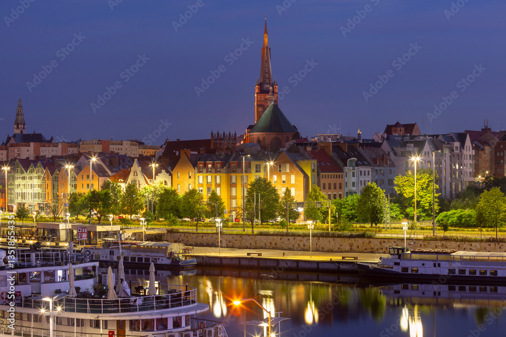 Oder River waterfront in Szczecin Poland with illuminated buildings and docked boats before sunrise