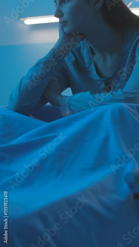 Young patient sitting on a hospital bed at night and feeling sad. Vertical video