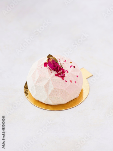 Crafted with artistry, this enchanting dessert features a geometric shape adorned with rose petals and delicate accents. A sweet indulgence capturing elegance and flavor