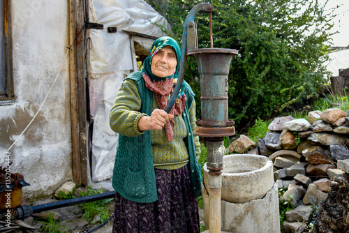 alte Frau füllt Wasser aus Pumpe in Eimer