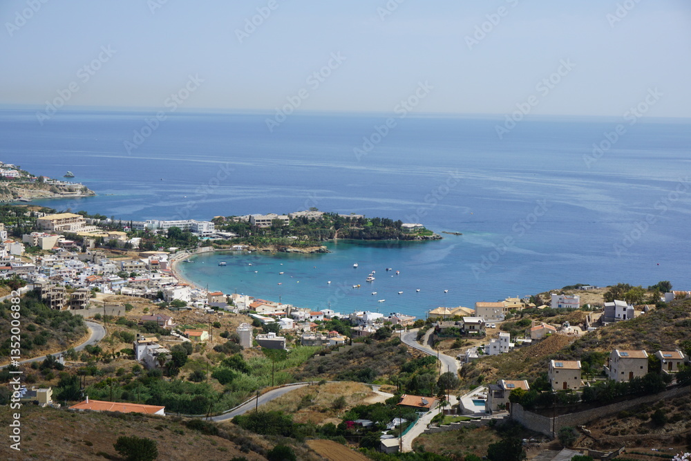 Naklejka premium Panoramic view of Agia Pelagia in Crete, Greece from above with the blue sea and the clear blue sky in the background - Holiday homes, villas and hotels with swimming pools amidst beautiful vegetation