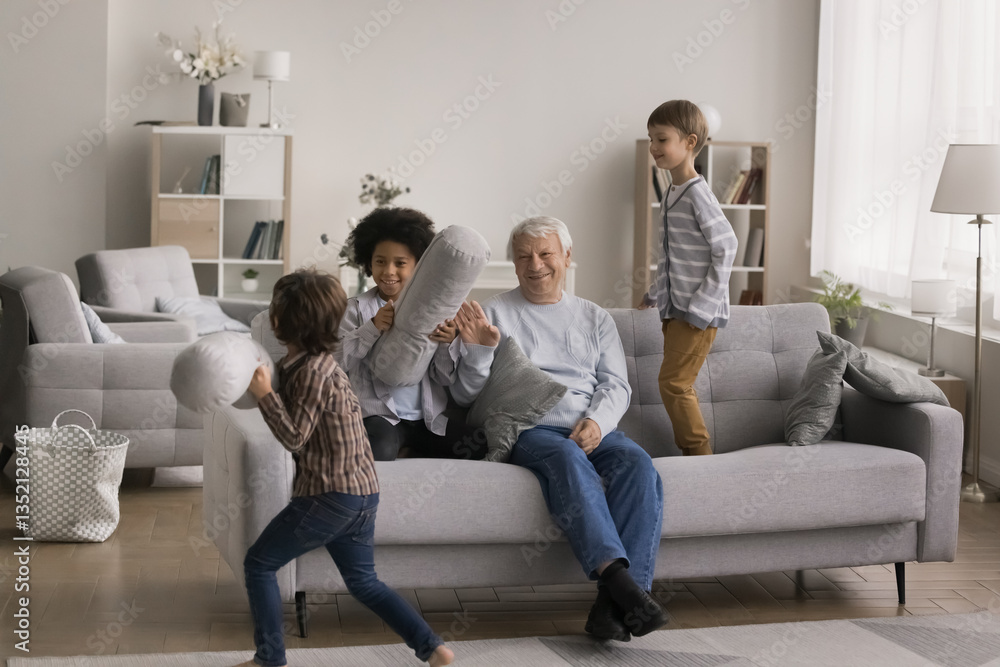 Grandpa support in mischief. Happy naughty kids friendly brothers preschoolers going crazy running jumping on sofa making fun pillow fight while smiling aged granddad watch and take part in funny mess Grandpa support in mischief. Happy naughty kids friendly brothers preschoolers going crazy running jumping on sofa making fun pillow fight while smiling aged granddad watch and take part in funny mess